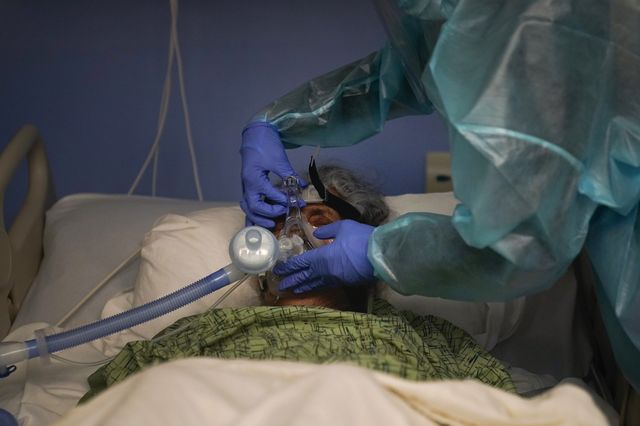 A patient wears a ventilator with a nurse's gloved hands adjusting it